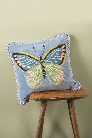 Decorative pillow with butterfly design on a wooden stool against a green wall
