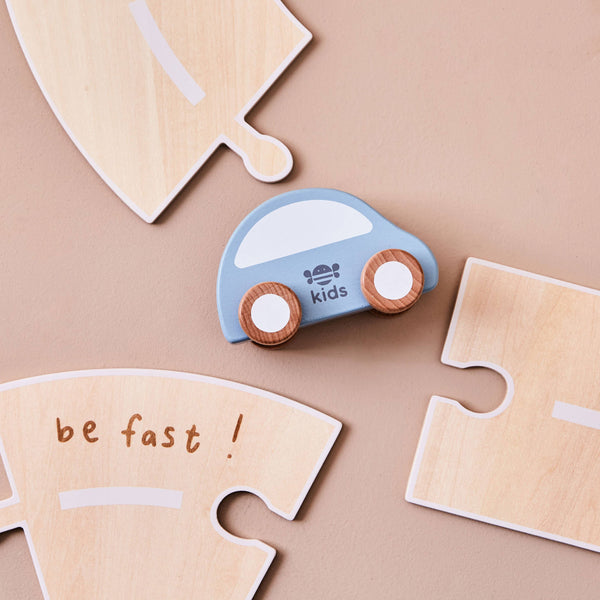Wooden toy car with 'kids' branding on a beige background with puzzle pieces.