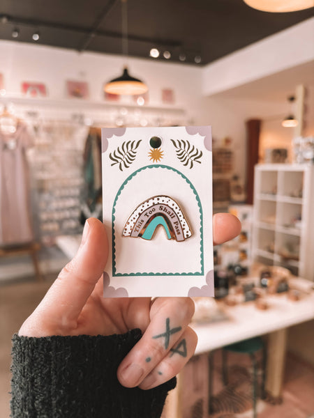 Hand holding a card with a decorative rainbow pin design in a store setting