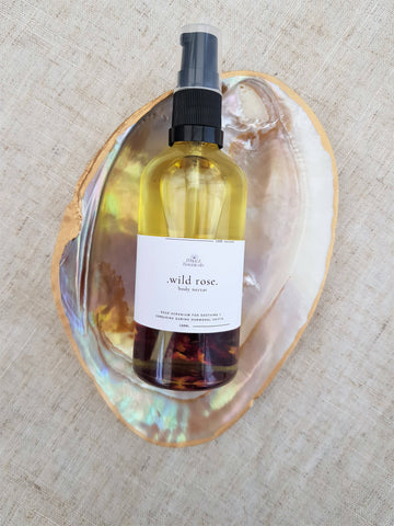Bottle of 'wild rose' body mist in a shell on a textured beige background