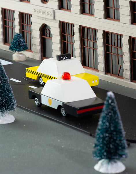 Model taxi and police car on a miniature street with buildings and trees in the background