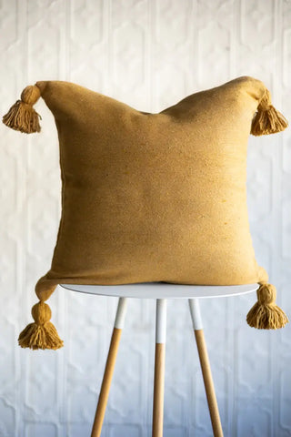 Mustard yellow cushion with tassels on a white table against a neutral background