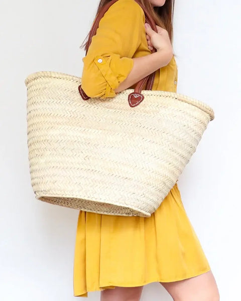 Person wearing a yellow outfit holding a large straw bag on a white background