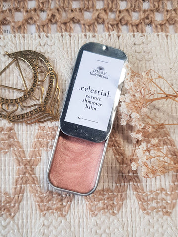 Cosmetic shimmer balm in a tin with 'celestial' label on textured fabric background