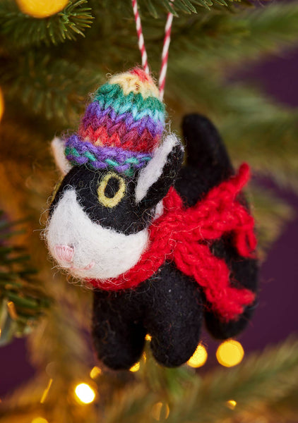 Knitted cat ornament with a colourful hat and red scarf hanging on a Christmas tree.