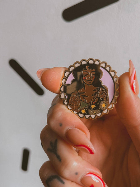 Hand holding a decorative badge with intricate design against a neutral background
