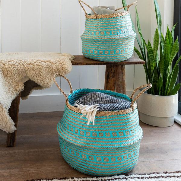 Two turquoise woven baskets with handles on a wooden surface, surrounded by a plant and a bench.
