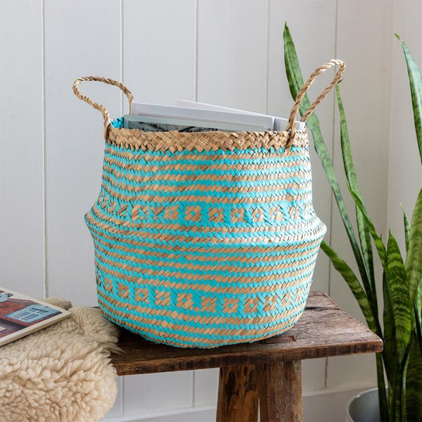 Woven basket with blue and beige pattern on a wooden stool against a white paneled wall.