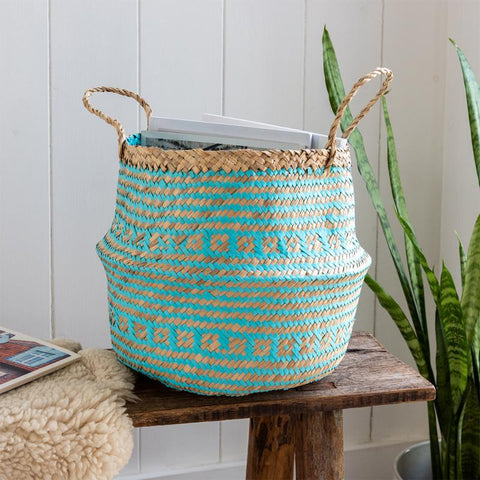 Woven basket with blue and beige pattern on a wooden stool against a white paneled wall.