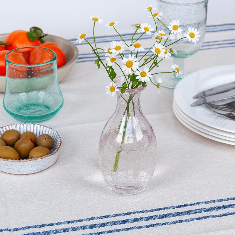 Clear glass vase with flowers on a table setting with plates, glasses, and fruit.