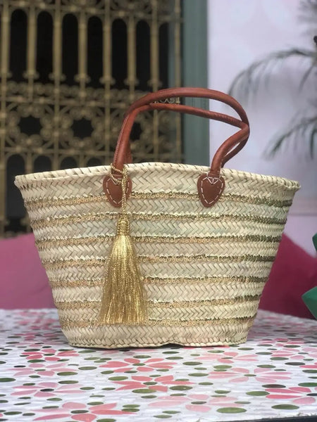 Woven straw bag with brown handles and tassel on a floral tablecloth