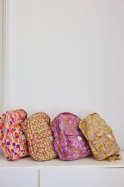 Four colourful backpacks arranged in a row against a white wall.