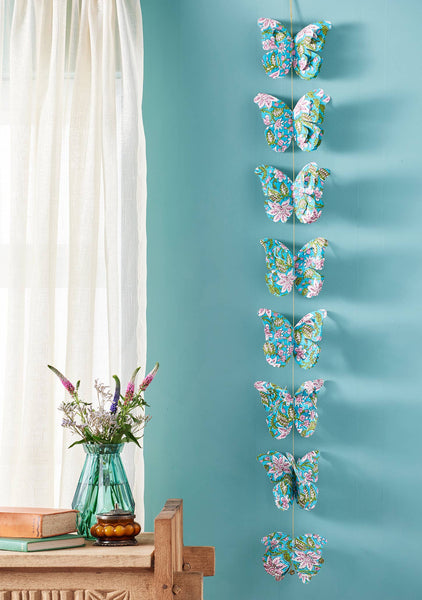 Decorative butterfly wall art on a blue wall with a vase of flowers and books on a table.
