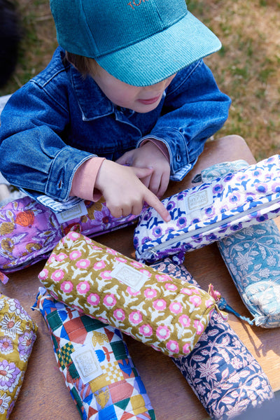 Child playing with colorful fabric pencil cases on a wooden surface