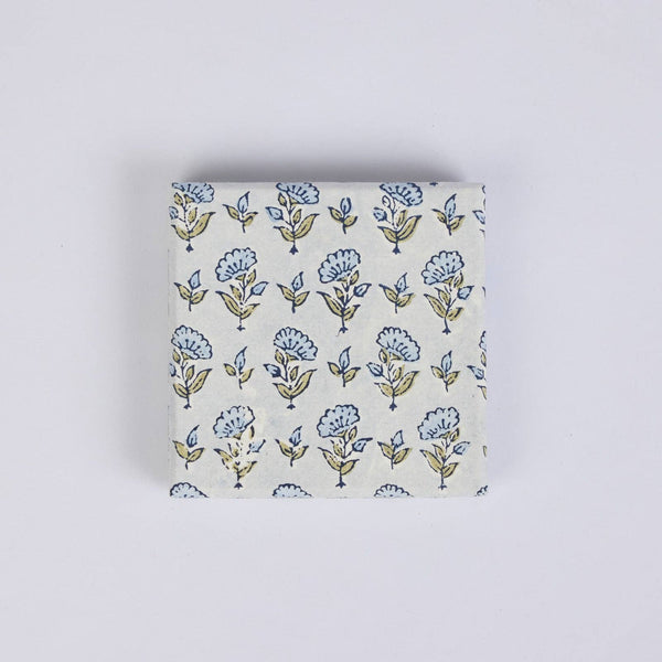 A decorative gift box featuring a delicate repeating floral block print in blue and green on a warm off-white background, set against a plain studio backdrop.