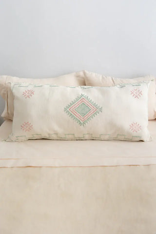 Decorative pillow with geometric pattern on a bed with beige bedding.