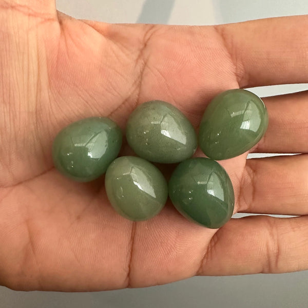 Four green gemstones held in a hand against a neutral background