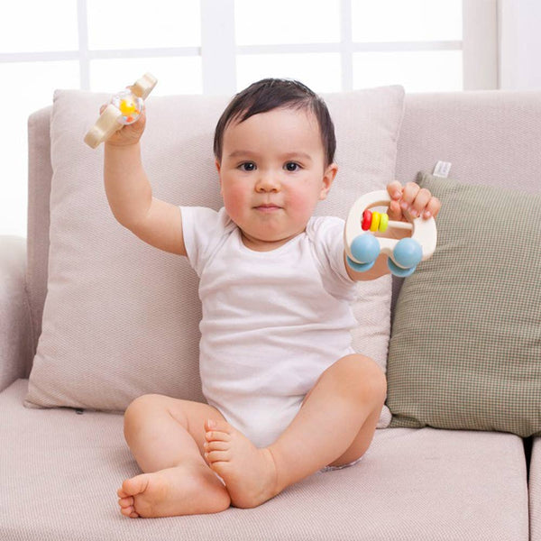 Baby sitting on a couch holding two toys, one in each hand.