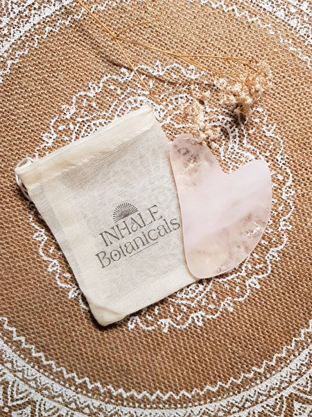 INHALE Botanicals gua sha board and pouch on a textured surface with a decorative border
