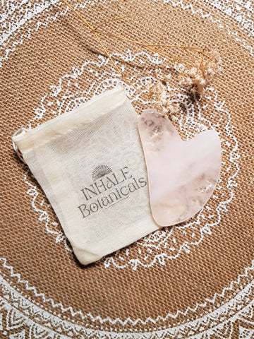 INHALE Botanicals gua sha board and pouch on a textured surface with a decorative border