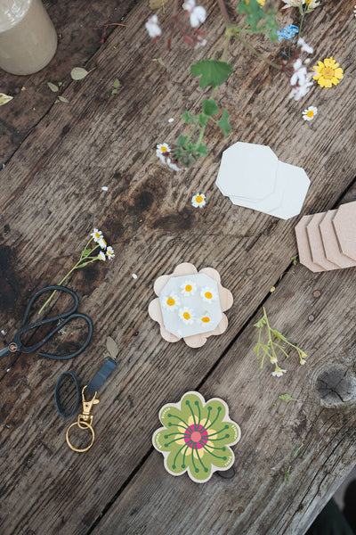 Mini flower presses on a wooden surface with scissors and flowers.