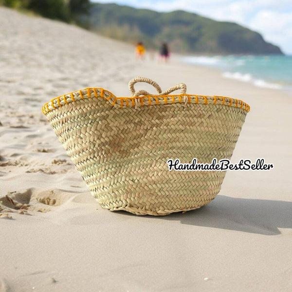 Woven basket with yellow rim on a sandy beach with people and mountains in the background