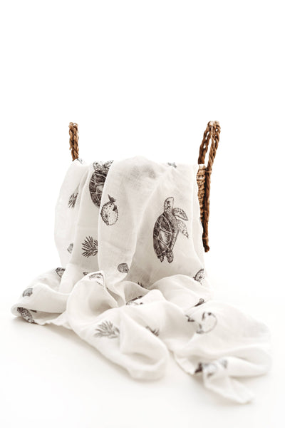 White fabric with turtle pattern draped over a woven basket on a white background
