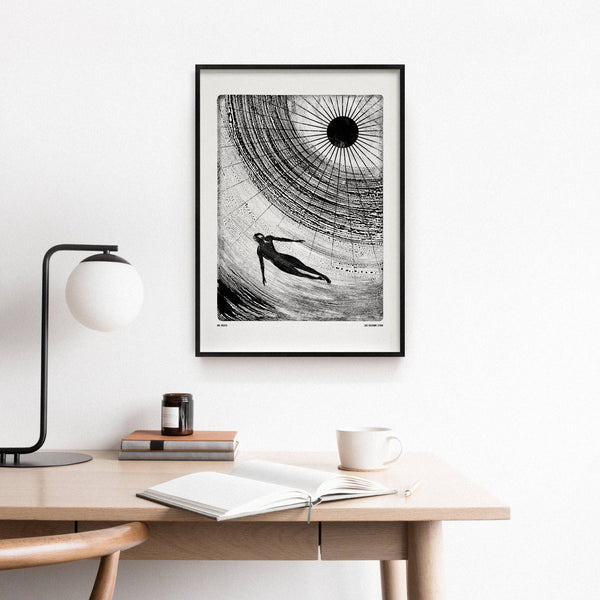 Framed black and white artwork on a wall above a desk with books and a lamp.