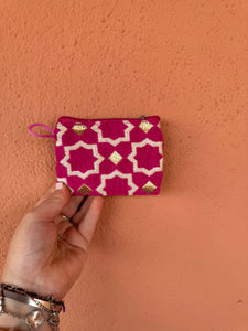 Hand holding a pink and white patterned pouch against an orange wall