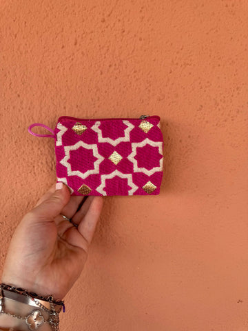 Hand holding a pink and white patterned pouch against an orange wall