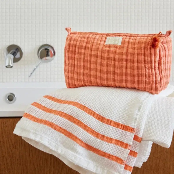 Orange checkered pouch and striped towel on a white surface with a tiled wall background
