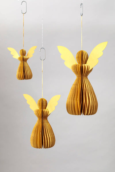 Three hanging paper angel ornaments in warm golden yellow and light yellow tones, suspended against a plain light grey background.