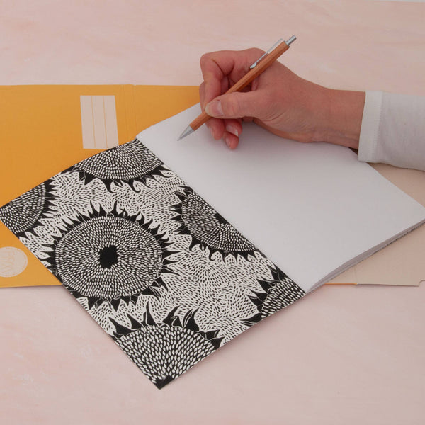 A person holding a pen, about to draw in a black and white sunflower print notebook