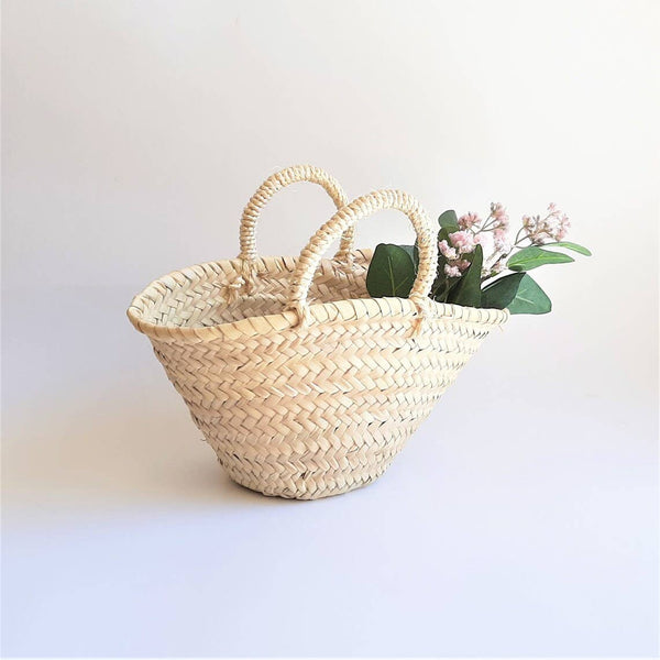 Woven basket with handles holding flowers on a light background