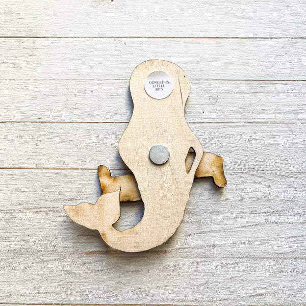 Back of a wooden mermaid magnet on a wooden surface