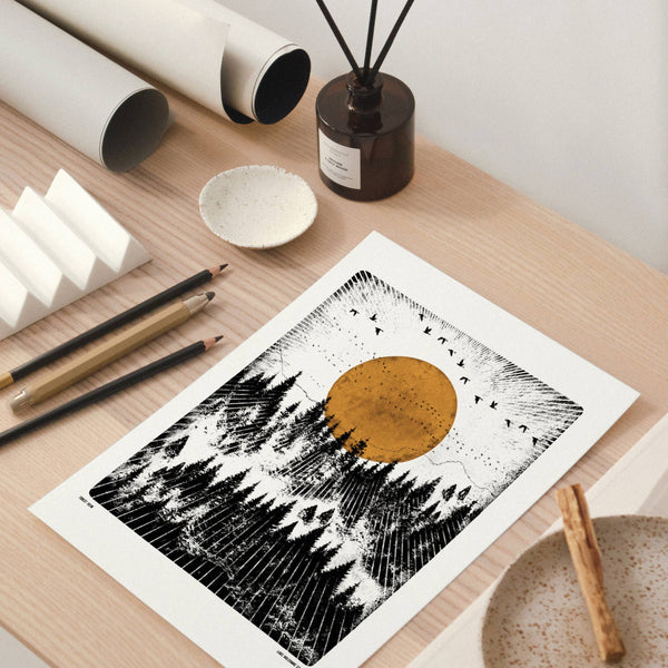 Art print of a mountain landscape with a brown circle on a wooden surface with stationery items.