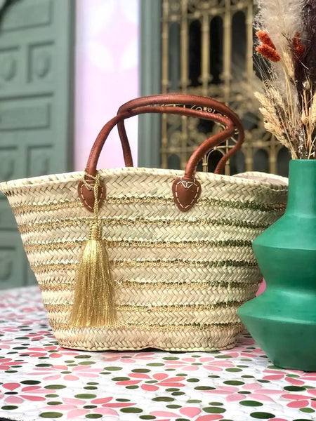 Woven straw bag with brown handles and gold tassel on a polka dot surface.