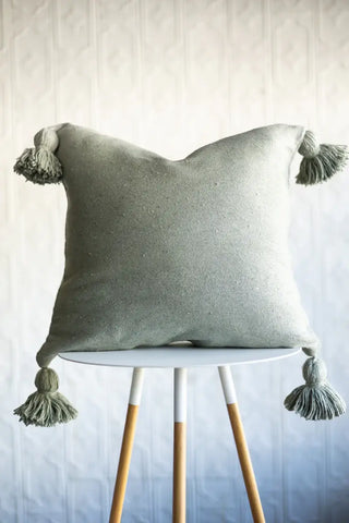 Green pillow with tassels on a white stool against a light wooden panel background