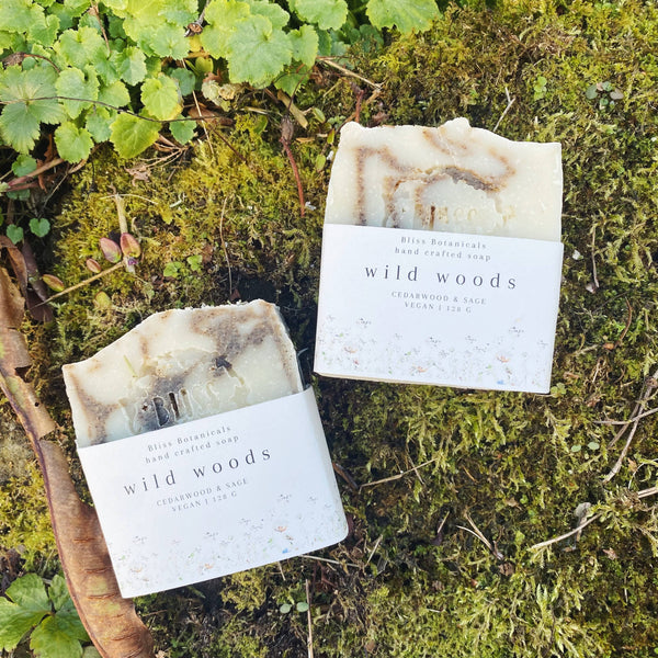 Two bars of 'wild woods' soap on a mossy surface with greenery.