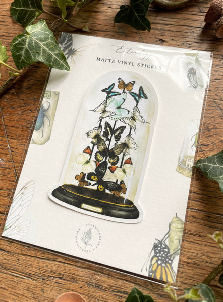 Packaging of butterfly-themed matte vinyl stickers on a wooden surface with green leaves.