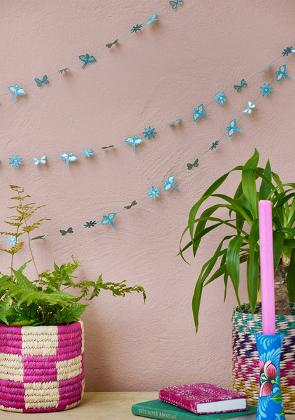 Decorative butterfly garland on a pink wall with plants and books on a table.