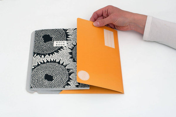 Person opening an orange folder with a black and white patterned notebook next to it on a white surface.