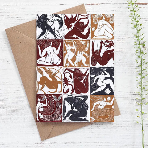 Card with zodiac sign illustrations on a white wooden surface with a brown envelope.