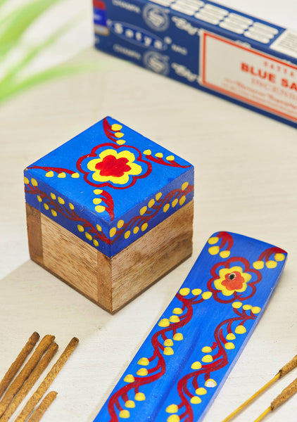 Decorative wooden box with blue lid featuring a floral design, placed on a light surface.