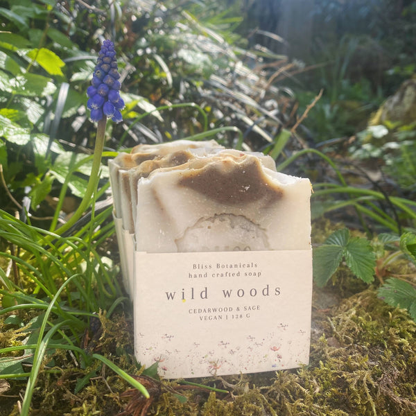 Handcrafted soap bar labeled 'wild woods' in a natural setting with greenery and a blue flower.