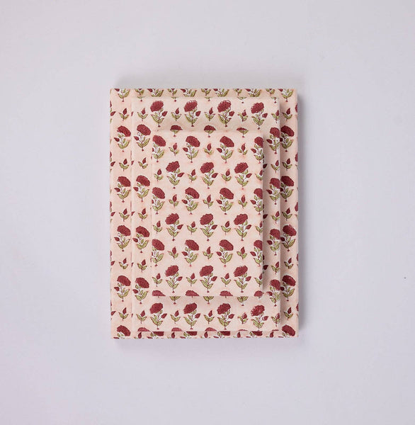 Three stacked rectangular gift boxes in a stack, featuring a repeating pattern of red flowers and green leaves on a light pink background, laid flat on a light grey surface.