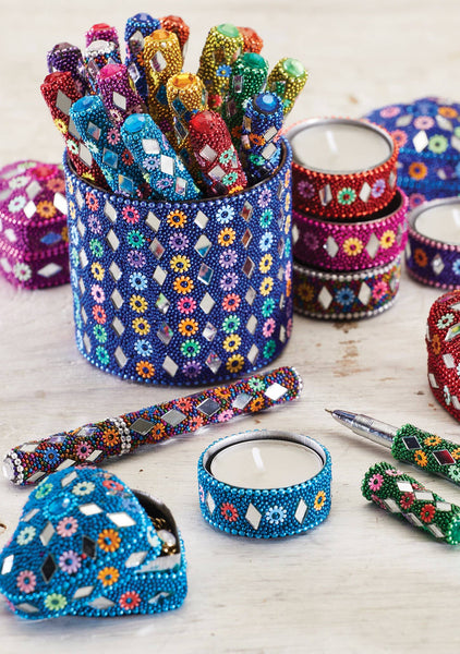 Colourful beaded pens, candles and decorative pots on a wooden surface