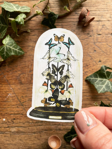 Decorative card with butterfly design held by a hand on a wooden surface with ivy leaves.