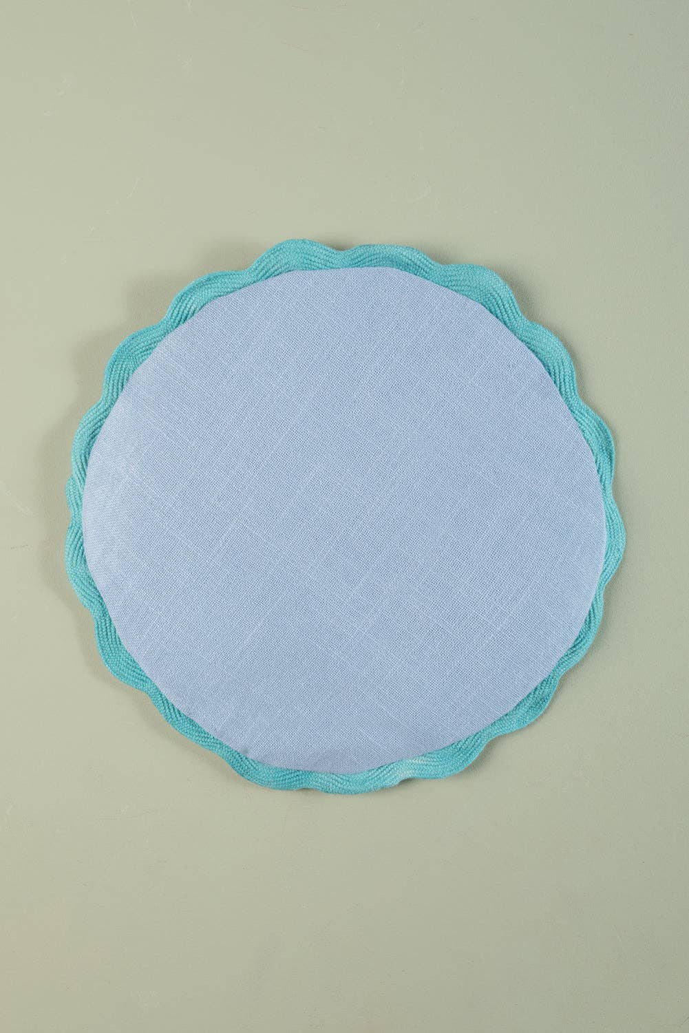 Round light blue cushion with turquoise rim on a beige background