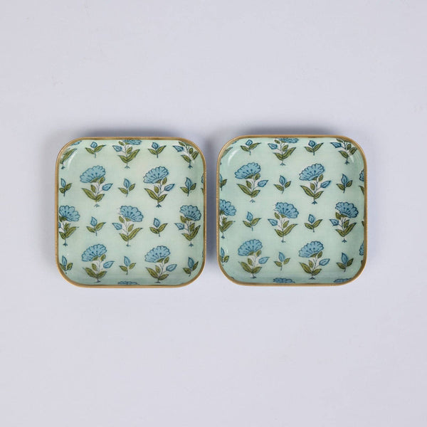 Two small square ceramic dishes with rounded corners, featuring a light mint green background decorated with a repeating blue and green floral pattern and a thin gold-toned rim, shown on a plain light grey background.